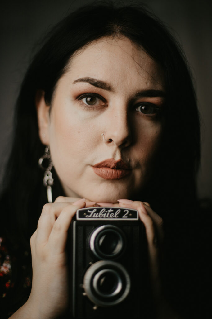 52 week photography challenge: self portrait. A woman looking at the camera, holding a vintage Lubitel camera.
