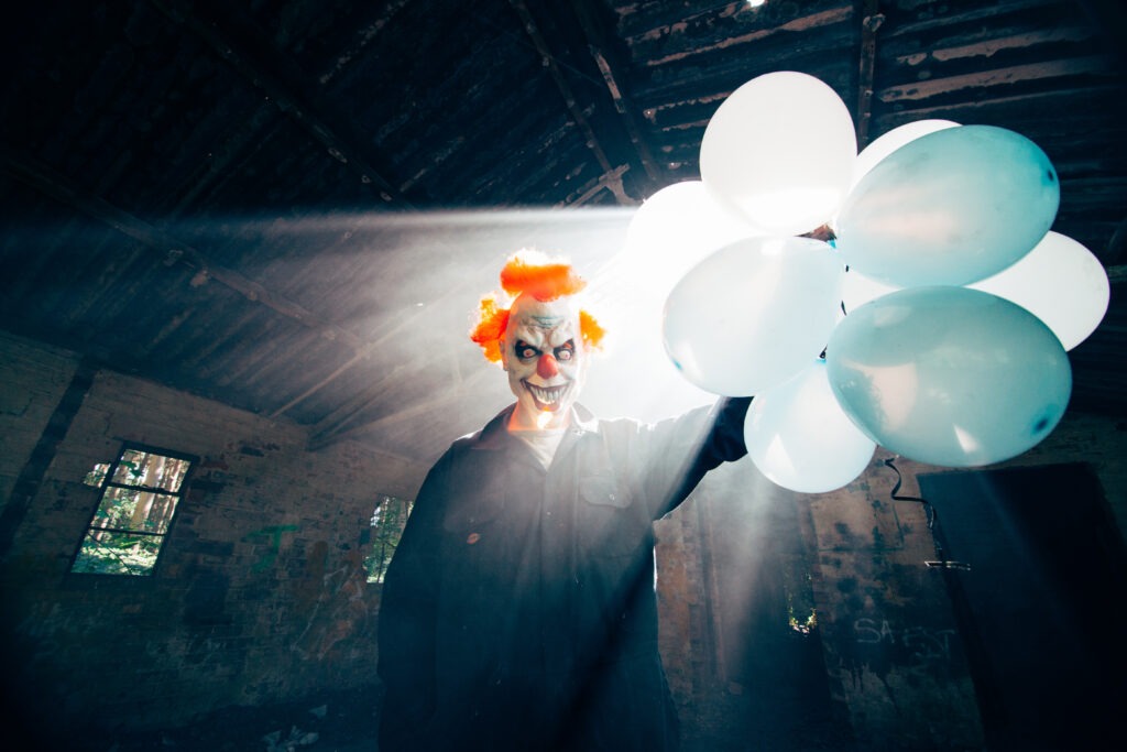 Halloween photography ideas: A clown holding balloons with rays of light behind him.