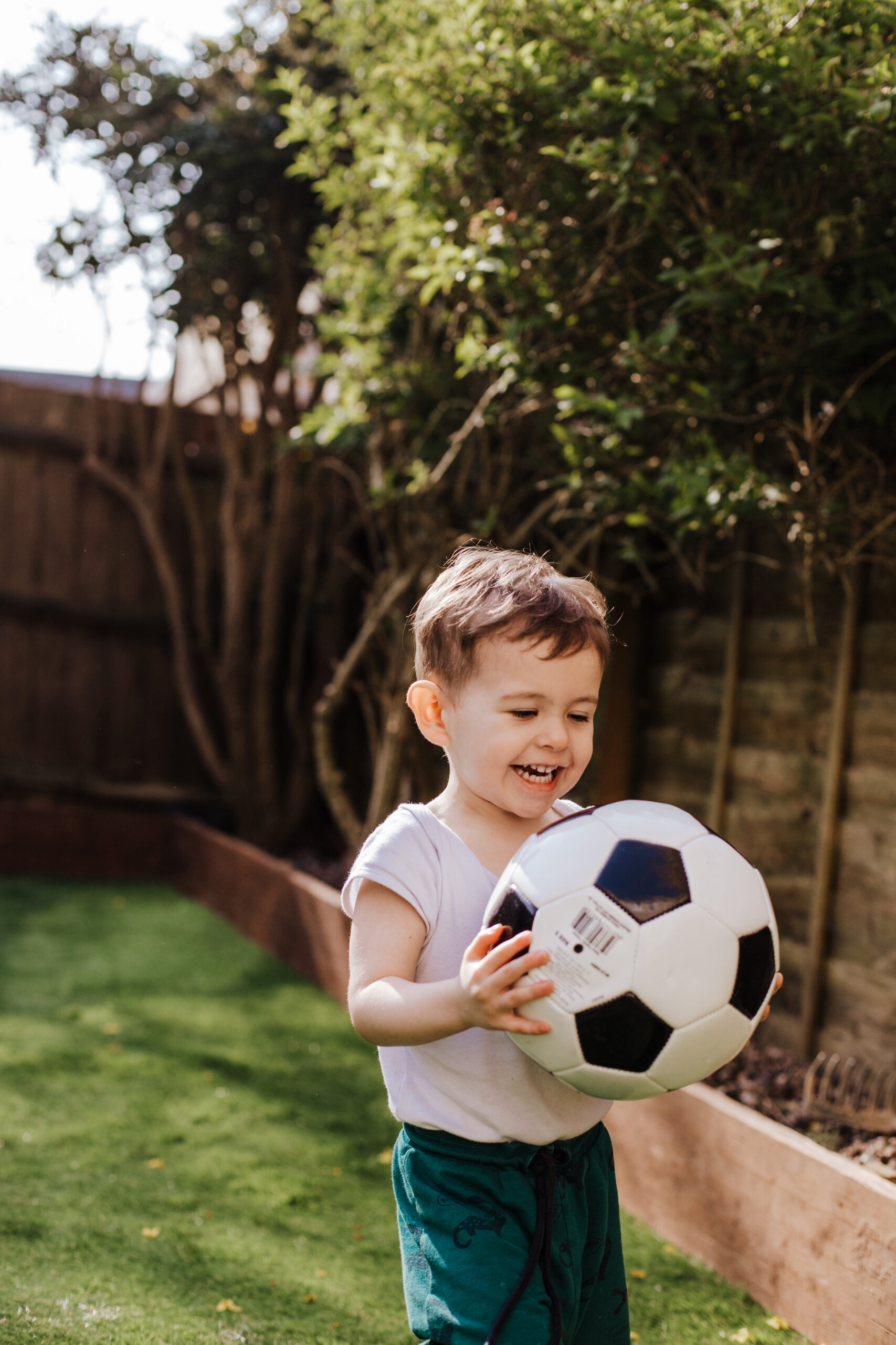 Photograph of a kid in the back garden, holding a football