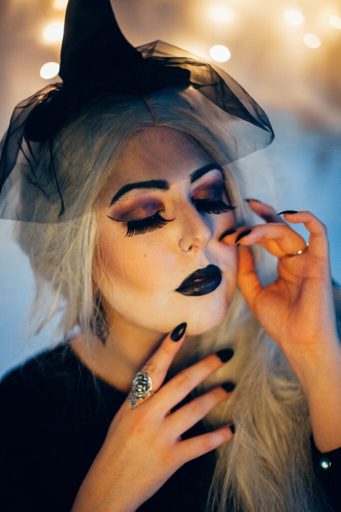 self portrait with bokeh lights in the background. Woman with black lipstick, long black nails, long grey hair and big eyelashes.