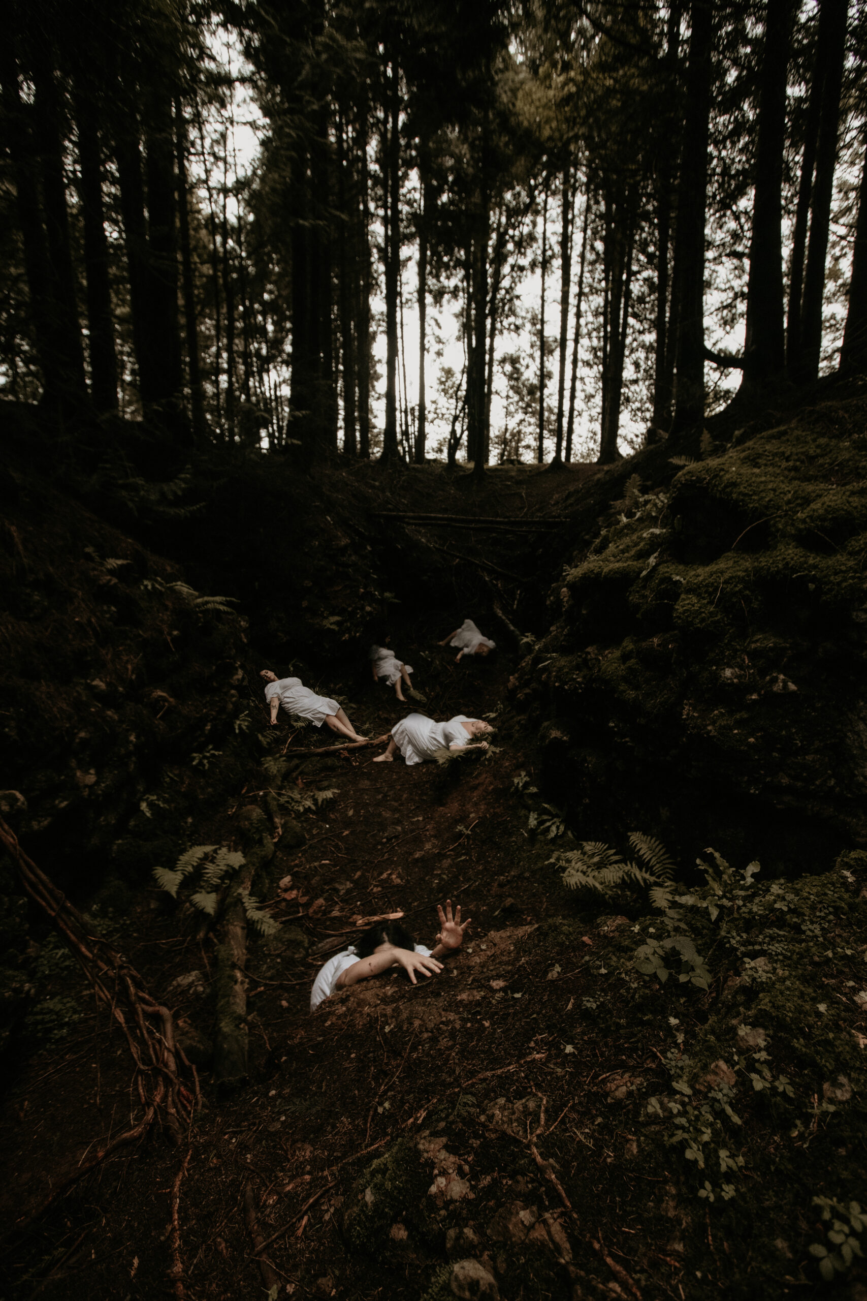 Conceptual self portrait of women in white dresses laying in a ditch in the forest