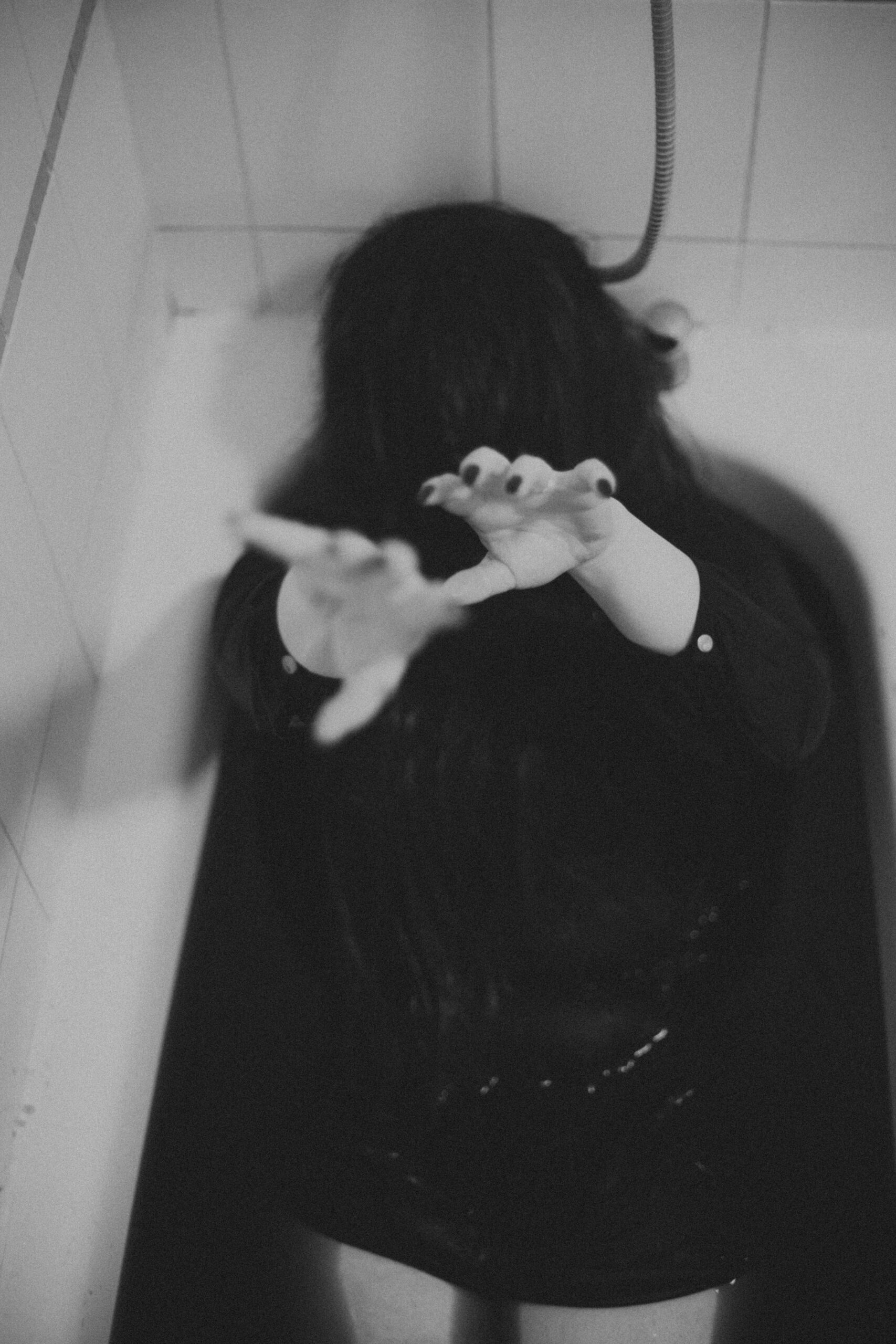 A black and white creepy photo of a woman with long black hair covering her face, reaching her hands out in a bath of blood
