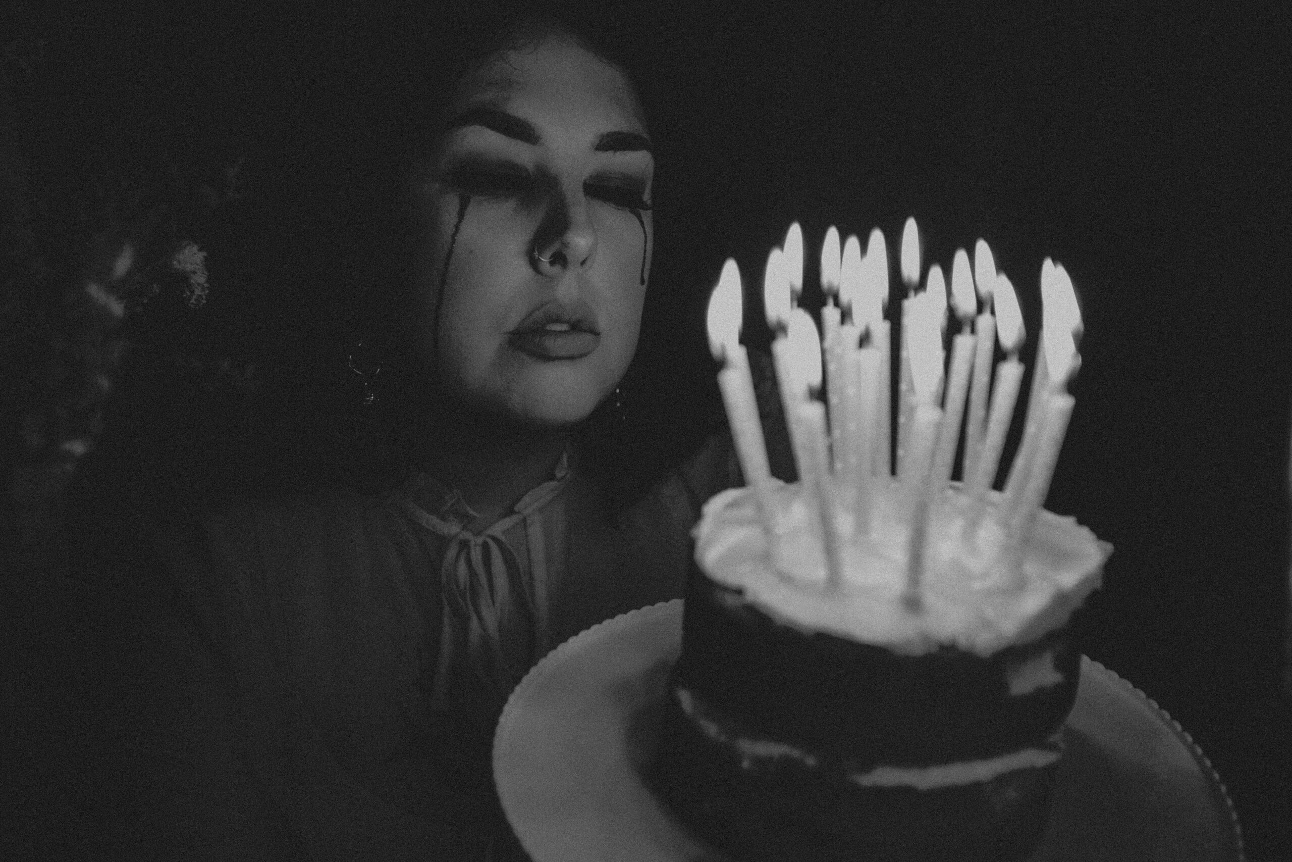 Black and white conceptual self portrait of a woman with bleeding eyes crying with a birthday cake and candles in front of her