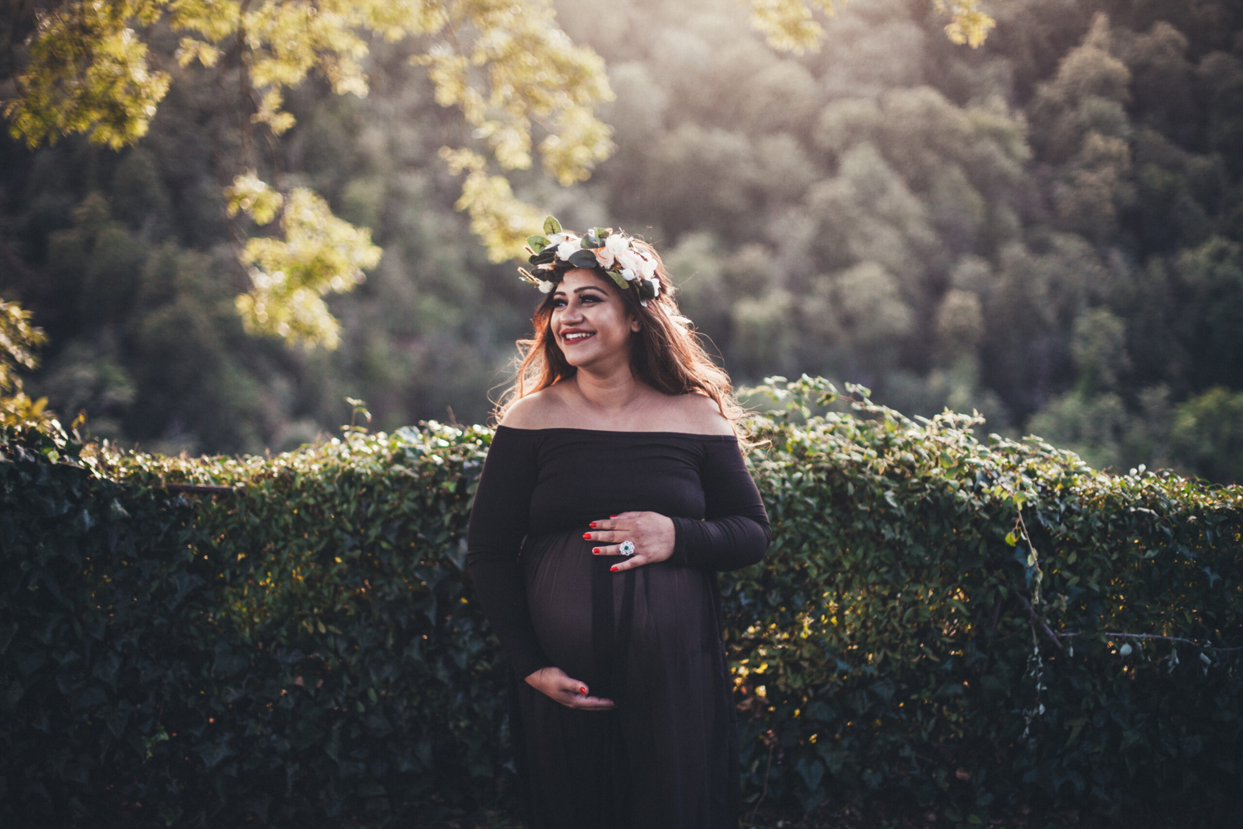 Maternity photo of a woman in a flower crown, long sheer dress with trees in the background