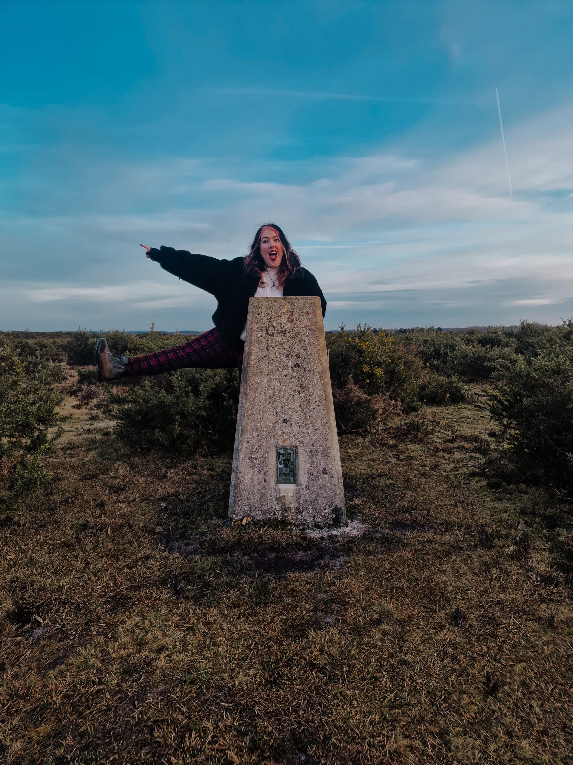 Hiker with pink hair and tartan leggings at a trig in the new forest
